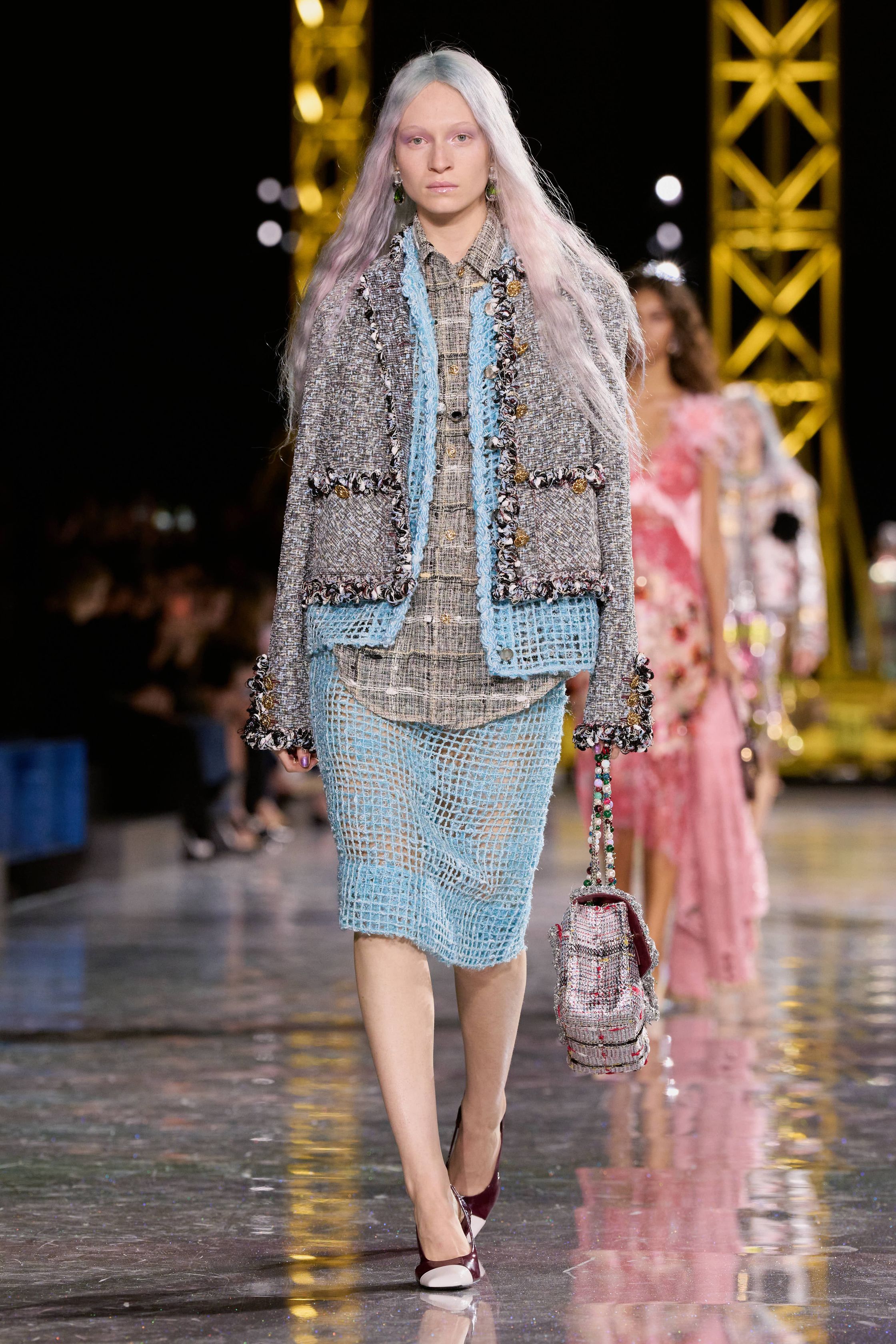 Chanel 2026秋冬在金属结构的秀场中重申品牌经典语言：斜纹软呢套装、短外套、膝下裙与珍珠配饰贯穿始终，柔粉、米色、黑白格纹与酒红色调构建出典型的巴黎优雅衣橱。本季轮廓更偏向轻松化比例，短夹克与宽松半裙形成现代化节奏，粗花呢被重新演绎为更轻盈的织物结构，同时融入羽毛、透明层纱与亮片细节，使经典香奈儿套装在年轻语境下焕发新的活力-顽石频道趋势研究